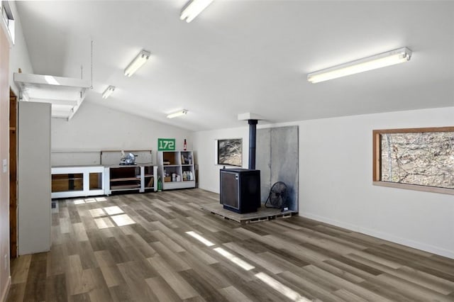 interior space with vaulted ceiling, a wood stove, wood finished floors, and baseboards