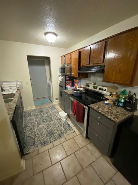 kitchen featuring under cabinet range hood, washer / clothes dryer, a textured ceiling, stainless steel appliances, and brown cabinetry