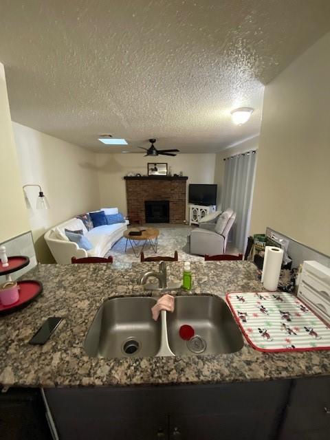 kitchen featuring stone counters, a fireplace, a textured ceiling, a ceiling fan, and a sink