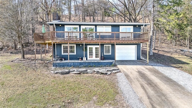 view of front of house featuring a deck, driveway, french doors, an attached garage, and a chimney