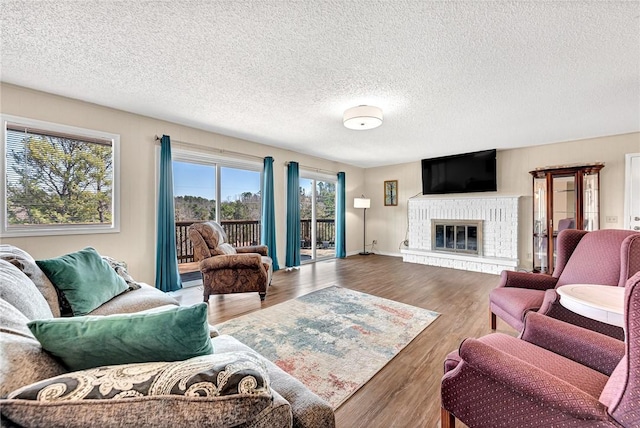 living area with a fireplace, a textured ceiling, baseboards, and wood finished floors