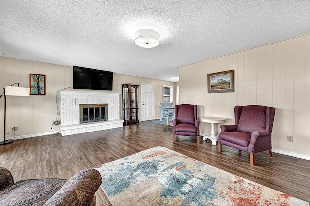 living area with a brick fireplace, wood finished floors, baseboards, and a textured ceiling