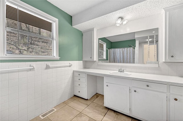 bathroom with visible vents, a textured ceiling, tile walls, wainscoting, and vanity