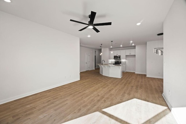 unfurnished living room featuring a sink, recessed lighting, light wood-style floors, baseboards, and ceiling fan