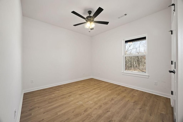 empty room with a ceiling fan, wood finished floors, visible vents, and baseboards