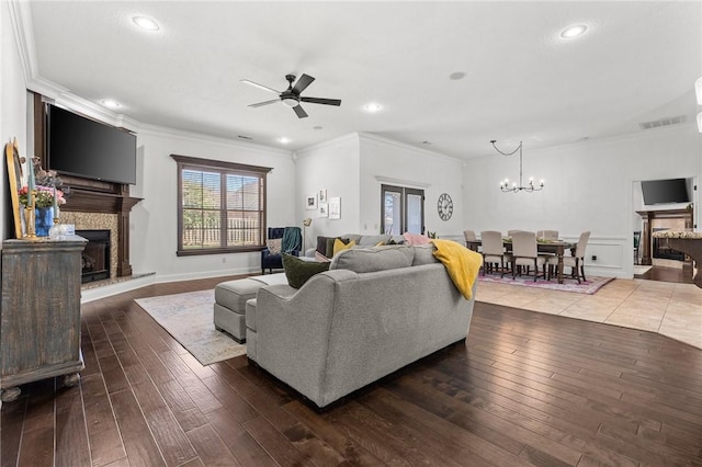 living room with ceiling fan with notable chandelier, crown molding, a fireplace with raised hearth, and wood-type flooring