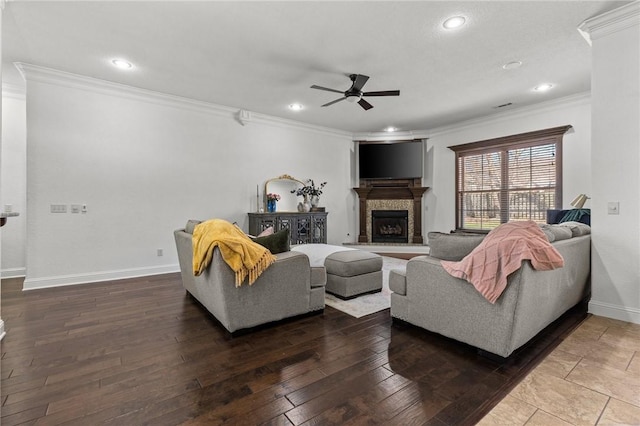 living area featuring baseboards, a fireplace with raised hearth, ornamental molding, ceiling fan, and wood-type flooring