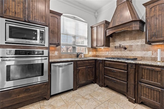 kitchen with crown molding, custom range hood, decorative backsplash, appliances with stainless steel finishes, and a sink