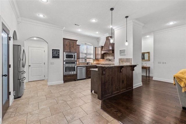 kitchen featuring visible vents, premium range hood, a peninsula, stainless steel appliances, and a kitchen bar