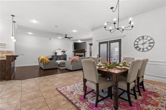 dining area featuring tile patterned flooring, ceiling fan with notable chandelier, a tile fireplace, and crown molding