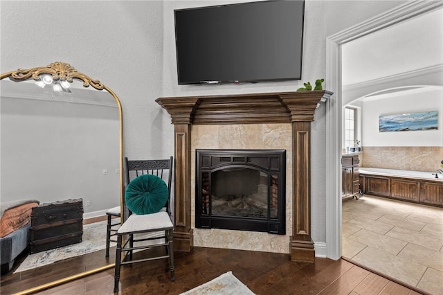 interior space featuring arched walkways, wood finished floors, a fireplace, and crown molding