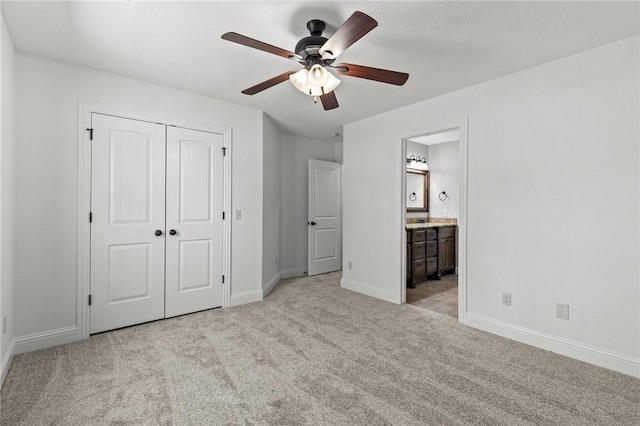 unfurnished bedroom with baseboards, light colored carpet, a closet, ensuite bath, and a ceiling fan