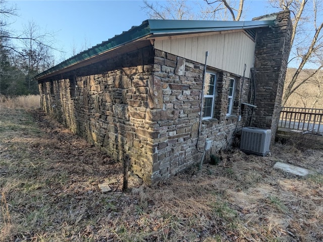 view of side of property with central AC unit, stone siding, and metal roof