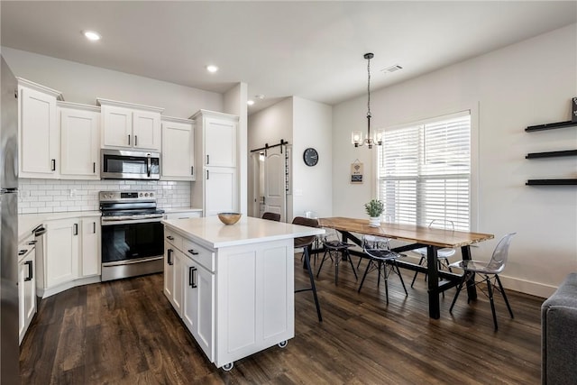 kitchen with stainless steel appliances, light countertops, dark wood-type flooring, a barn door, and tasteful backsplash