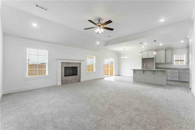 unfurnished living room featuring visible vents, ceiling fan with notable chandelier, a sink, light colored carpet, and a tile fireplace