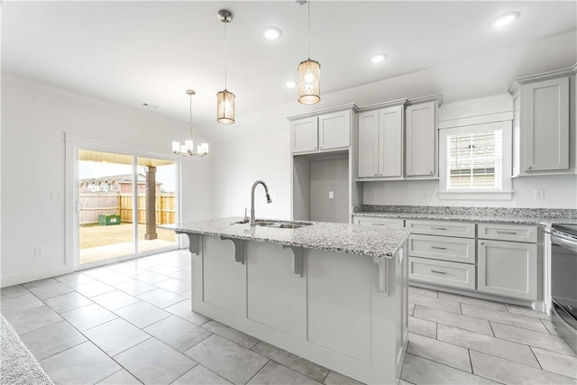 kitchen featuring a sink, plenty of natural light, light stone counters, and an island with sink