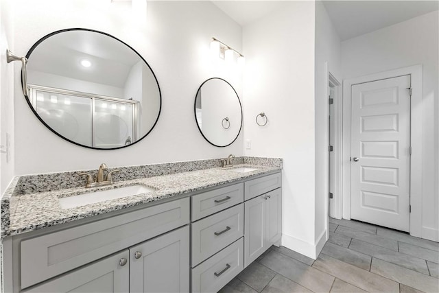 full bathroom with double vanity, an enclosed shower, baseboards, and a sink