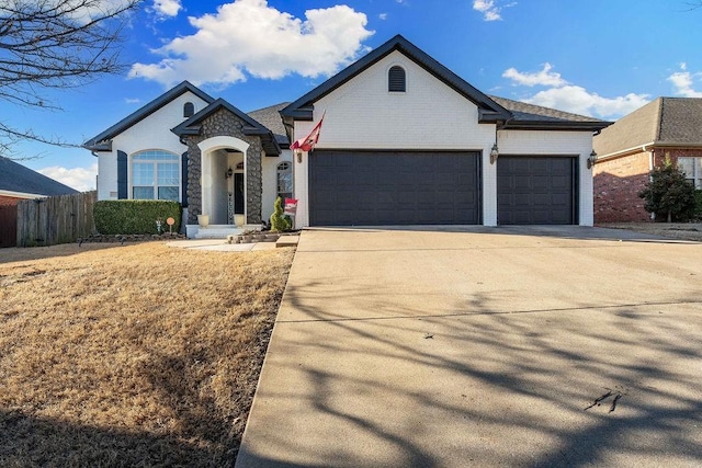 view of front facade featuring stone siding, an attached garage, driveway, and fence