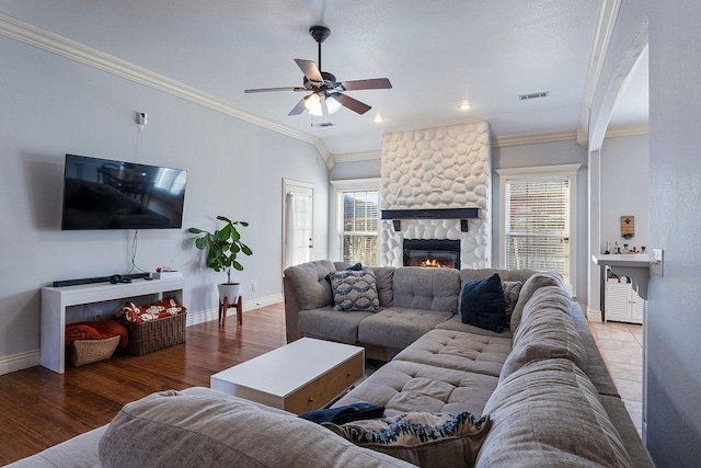 living area with visible vents, crown molding, a fireplace, wood finished floors, and a ceiling fan