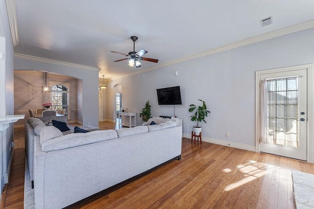 living area featuring a ceiling fan, visible vents, baseboards, arched walkways, and hardwood / wood-style flooring