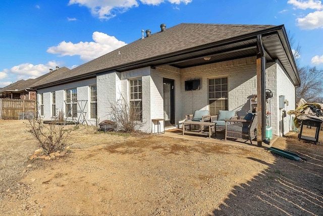 back of property featuring brick siding, a shingled roof, and fence