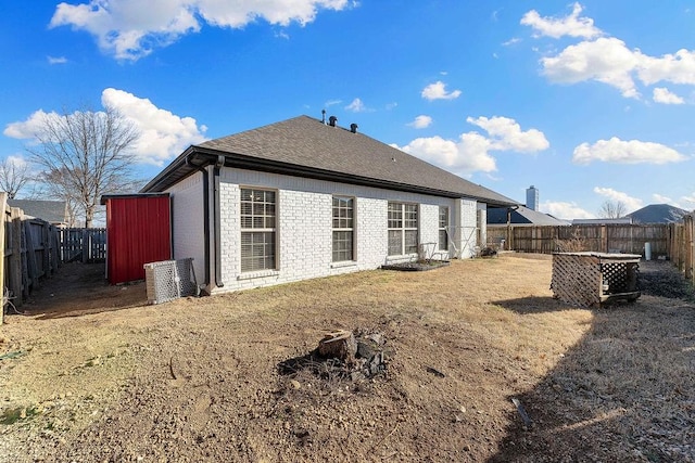 rear view of house featuring a fenced backyard, brick siding, and roof with shingles