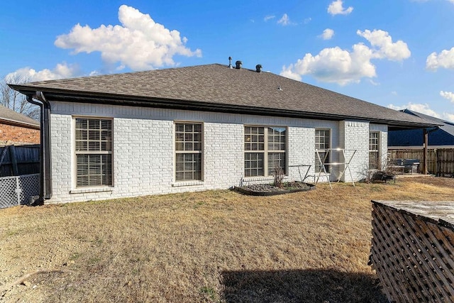 back of property with a lawn, roof with shingles, and fence