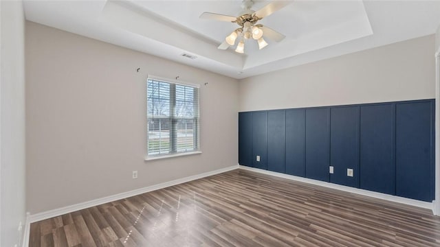 empty room featuring visible vents, wood finished floors, baseboards, a raised ceiling, and ceiling fan