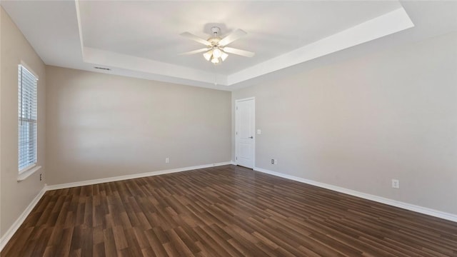 empty room featuring dark wood finished floors, baseboards, a tray ceiling, and a ceiling fan