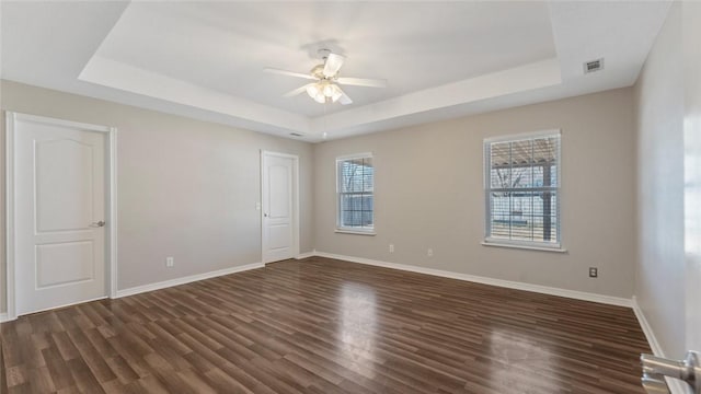 empty room with visible vents, dark wood-type flooring, a raised ceiling, and ceiling fan