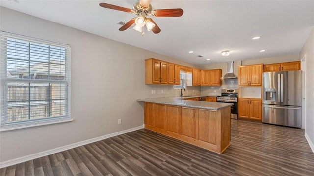 kitchen featuring tasteful backsplash, appliances with stainless steel finishes, a peninsula, wall chimney range hood, and baseboards