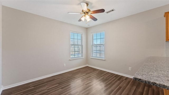 spare room with visible vents, baseboards, dark wood-style floors, and a ceiling fan