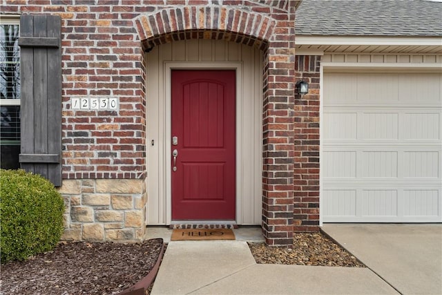 property entrance with a garage, brick siding, and roof with shingles