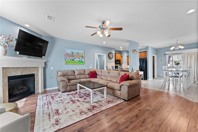 living area featuring visible vents, baseboards, light wood-type flooring, ceiling fan with notable chandelier, and a tile fireplace