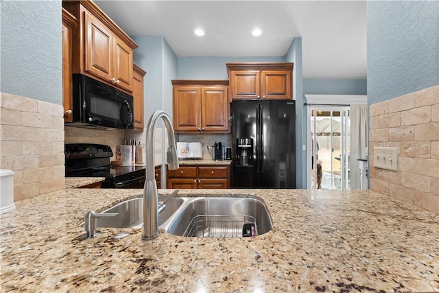 kitchen with light stone countertops, a sink, black appliances, brown cabinets, and backsplash