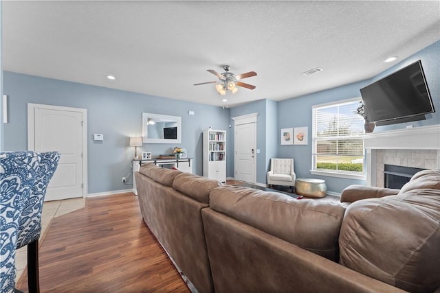 living area featuring wood finished floors, visible vents, baseboards, ceiling fan, and a tile fireplace