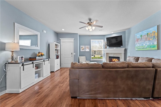 living area featuring a glass covered fireplace, wood finished floors, recessed lighting, baseboards, and ceiling fan