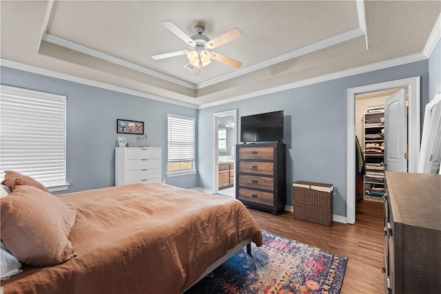 bedroom featuring a spacious closet, light wood finished floors, crown molding, and a tray ceiling