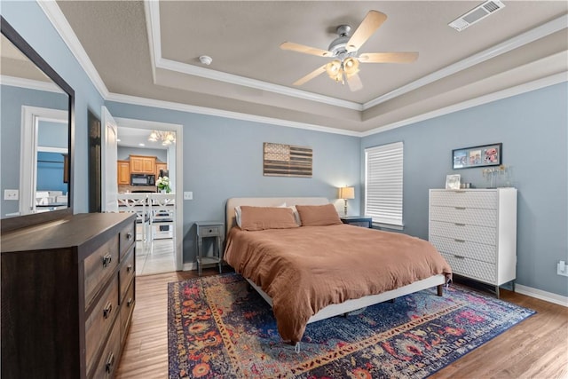 bedroom with visible vents, a tray ceiling, crown molding, light wood finished floors, and baseboards