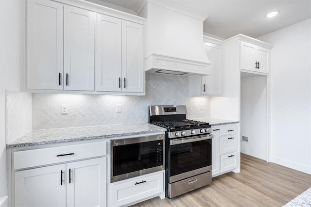 kitchen with stainless steel gas range oven, premium range hood, light stone counters, light wood finished floors, and built in microwave