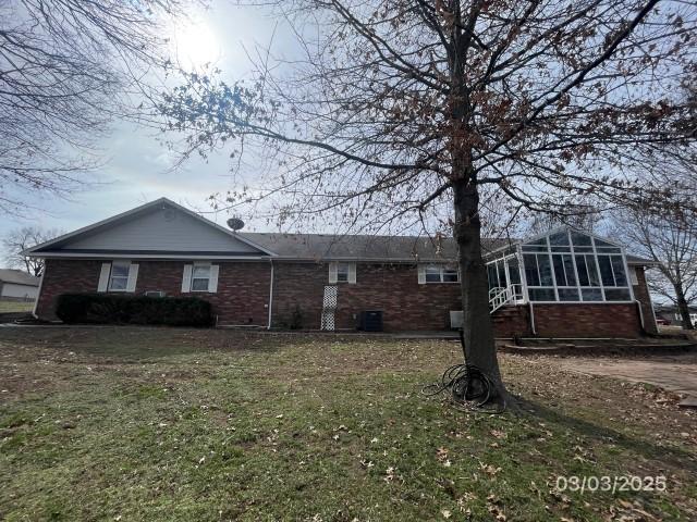 ranch-style home featuring brick siding, a front yard, and a sunroom