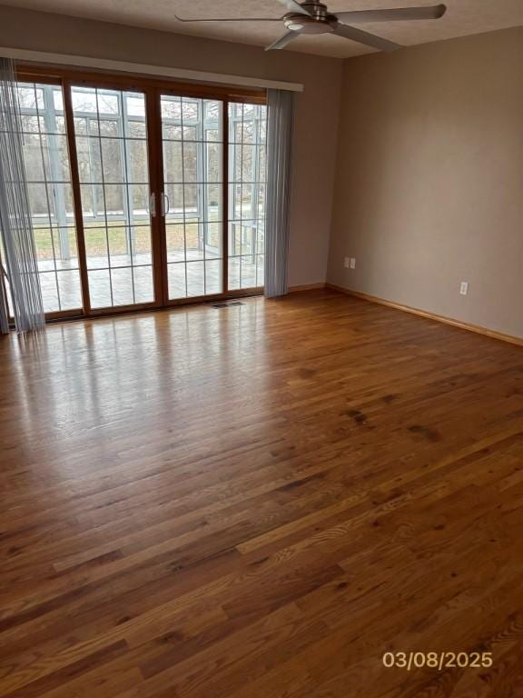 empty room with wood finished floors, a ceiling fan, and baseboards