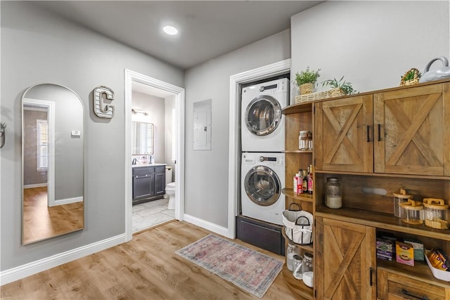 laundry area with arched walkways, light wood-style floors, stacked washer / drying machine, baseboards, and laundry area