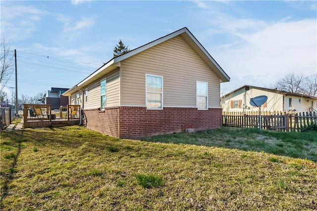 view of side of property featuring brick siding, a lawn, a wooden deck, and fence