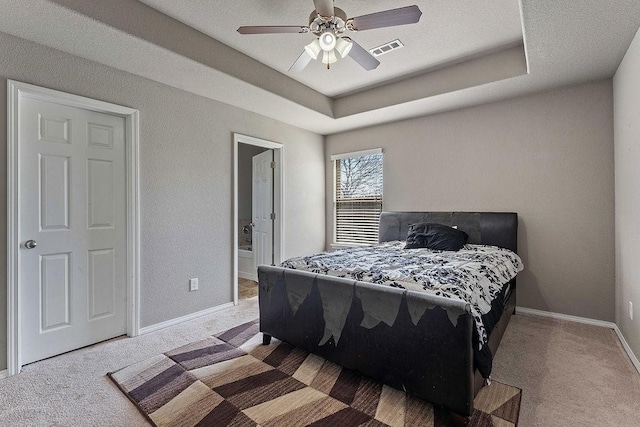 carpeted bedroom with visible vents, connected bathroom, baseboards, a raised ceiling, and a ceiling fan