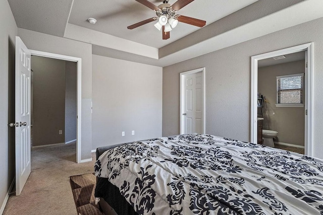 carpeted bedroom with a raised ceiling, baseboards, and ensuite bathroom