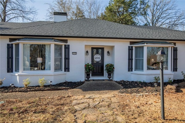 view of front of property featuring brick siding, roof with shingles, and a chimney