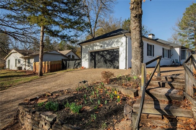 view of home's exterior featuring stucco siding, dirt driveway, fence, a garage, and a chimney