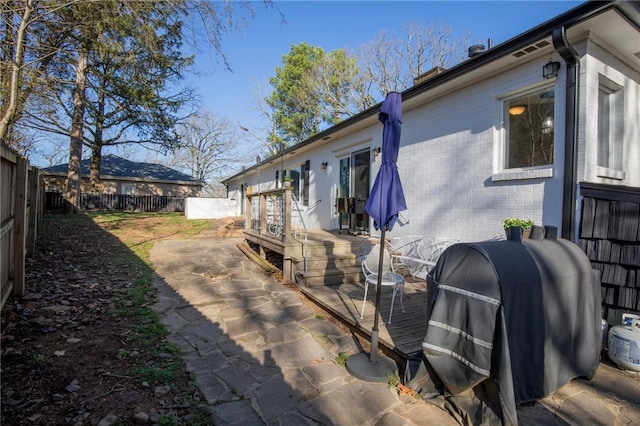 view of side of property featuring brick siding, a deck, a fenced backyard, a patio area, and heating fuel