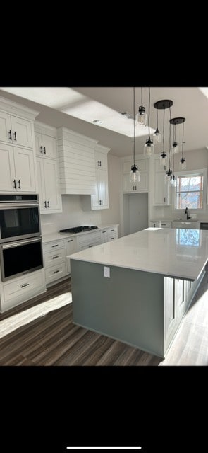 kitchen with a spacious island, wood finished floors, black stovetop, white cabinets, and light countertops